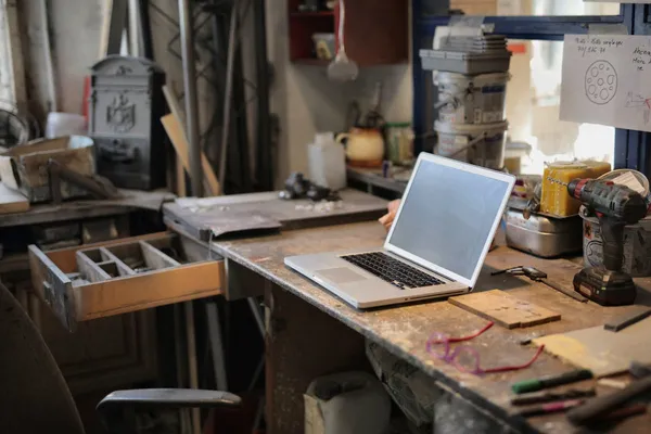 Laptop auf einer Werkbank in einer Handwerkswerkstatt mit Werkzeug im Hintergrund